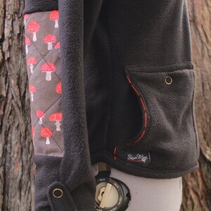May include: Black fleece jacket with a red mushroom pattern on the left sleeve. The jacket has a red stitched pocket on the right side with the text "Sew Much" in white.