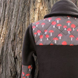 May include: A black fleece jacket with a gray and red mushroom pattern on the back and sleeves. The jacket has a high collar and a zipper closure.