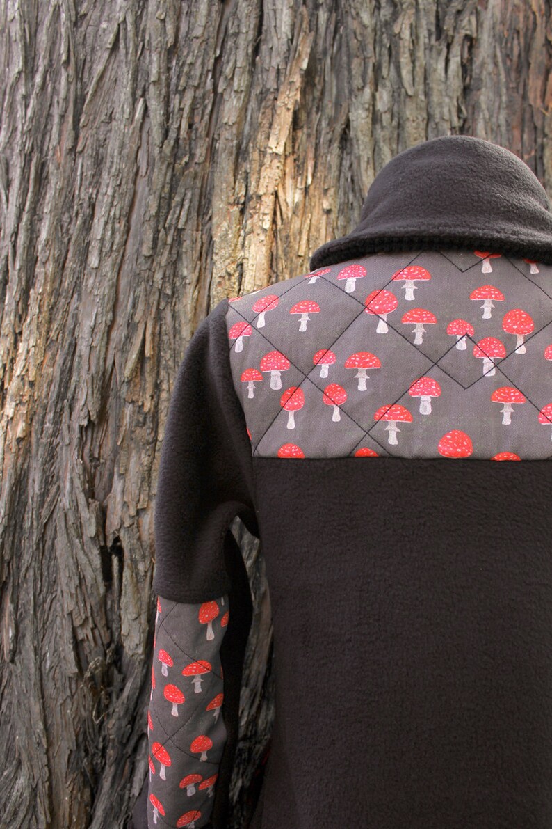 May include: A black fleece jacket with a gray and red mushroom pattern on the back and sleeves. The jacket has a high collar and a zipper closure.