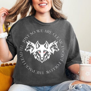 May include: Dark gray t-shirt with a white wolf graphic and the text "JUST SO WE ARE CLEAR, I DON'T FOLLOW THE PACK I LEAD IT!". The shirt is a short-sleeved, crew neck style.