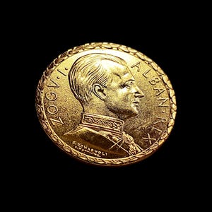 Peut inclure: Une pièce de monnaie dorée avec le profil d'un homme en uniforme militaire. La pièce porte des inscriptions sur le bord, dont le mot "ALBANIE". Le fond est noir.
