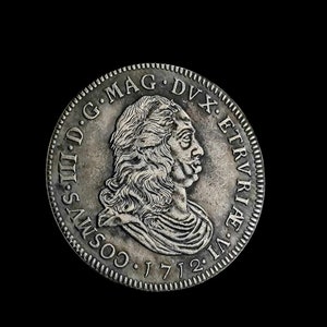Puede incluir: Moneda de plata con el retrato de un hombre con el pelo largo y barba. La moneda tiene la inscripción "COS. III. D. G. MAG. DVX. ETRURIAE" y la fecha "1712".