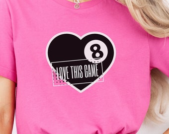 May include: A pink t-shirt with a black heart graphic featuring a white 8-ball and the text "LOVE THIS GAME".