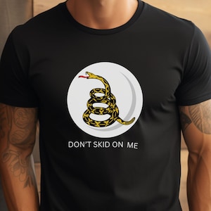 May include: A black t-shirt with a white circle and a yellow and black snake inside. The text "Don't Skid On Me" is printed below the circle.
