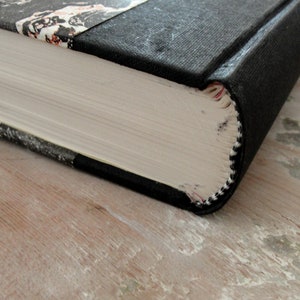 K&ouml;nnte beinhalten: Nahaufnahme des Buchr&uuml;ckens eines Hardcover-Buches mit einem schwarzen Stoffbezug und einem marmorierten Papierdesign auf dem vorderen Einband. Das Buch ist geschlossen und der R&uuml;cken ist sichtbar.