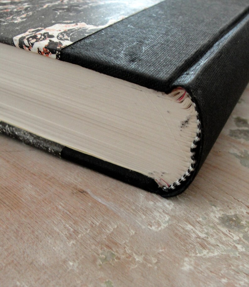 K&ouml;nnte beinhalten: Nahaufnahme des Buchr&uuml;ckens eines Hardcover-Buches mit einem schwarzen Stoffbezug und einem marmorierten Papierdesign auf dem vorderen Einband. Das Buch ist geschlossen und der R&uuml;cken ist sichtbar.