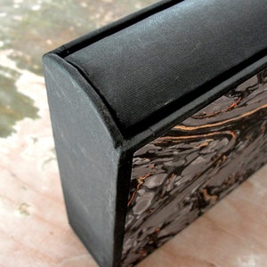 K&ouml;nnte beinhalten: Eine schwarze Box mit einem Marmormuster an der Seite. Die Oberseite der Box ist mit schwarzem Stoff bedeckt.