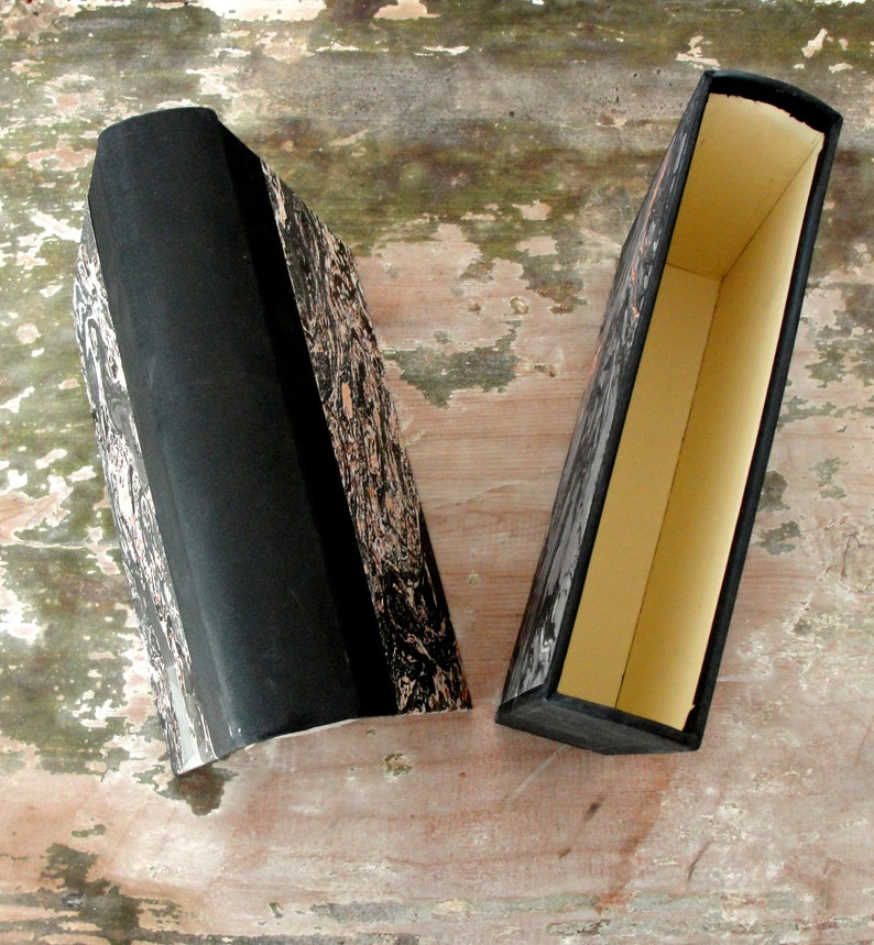 K&ouml;nnte beinhalten: Zwei schwarze Boxen mit einem Marmormuster auf der Au&szlig;enseite. Eine Box ist ge&ouml;ffnet und zeigt ein cremefarbenes Innenleben.