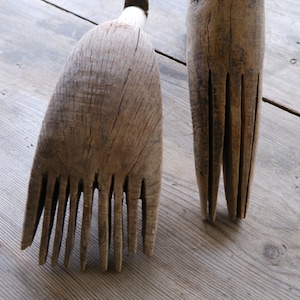 May include: Two wooden tools with multiple tines, resembling combs or rakes, are shown on a wooden surface. The tools are made of natural wood and have a rustic appearance.