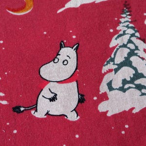 May include: A red fabric with a white Moomin character wearing a red scarf. The background has a white crescent moon, white snow, and a green and white tree.