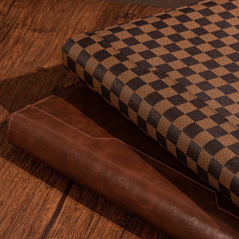 May include: A brown leather journal with a checkered brown and black cover on top of it.