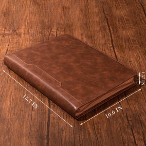 Pode incluir: Um portf&oacute;lio de couro marrom com z&iacute;per e fecho de aba. O portf&oacute;lio mede 34,8 cm por 26,9 cm.