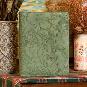 Puede incluir: Un diario de cuero verde con un diseño floral en relieve. El diario tiene una superficie texturizada y un brillo sutil.