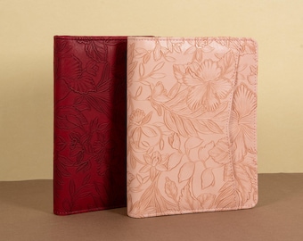 May include: Two leather journals with floral embossed designs. One journal is red and the other is pink.