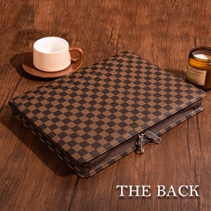 May include: A brown and black checkered zippered portfolio with a silver zipper pull. The back of the portfolio is shown in the image.