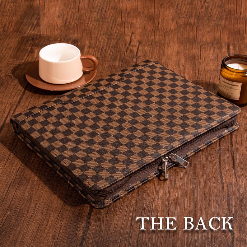 May include: A brown and black checkered zippered portfolio with a silver zipper pull. The back of the portfolio is shown in the image.