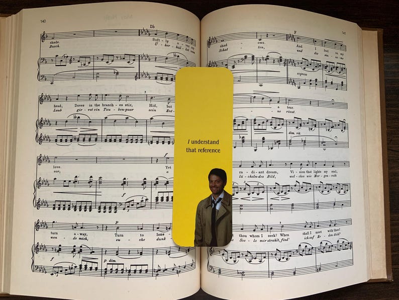May include: A yellow bookmark with the text "I understand that reference" and an image of a man in a coat, placed in an open book of sheet music. The book is open to a page of musical notation.