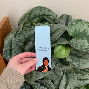 Op de afbeelding: Een rechthoekige lichtblauwe boekenlegger met een afbeelding van een man in een donkere jas en witte cravat. De tekst op de boekenlegger luidt: Hey girl, are you improving your mind by extensive reading? De boekenlegger heeft afgeronde hoeken.