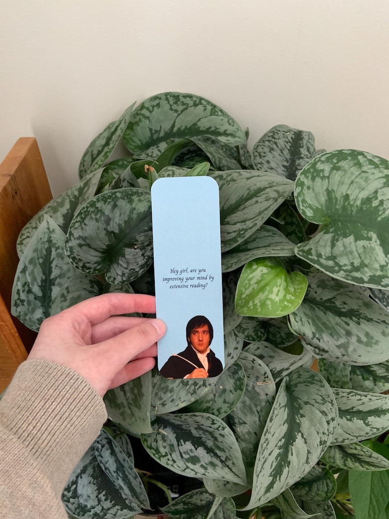 Op de afbeelding: Een rechthoekige lichtblauwe boekenlegger met een afbeelding van een man in een donkere jas en witte cravat. De tekst op de boekenlegger luidt: Hey girl, are you improving your mind by extensive reading? De boekenlegger heeft afgeronde hoeken.