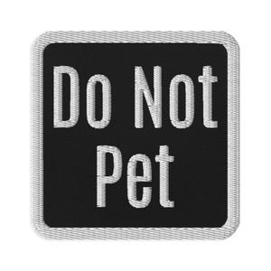 Pode incluir: Um remendo bordado preto e branco com o texto "Do Not Pet" em letras brancas.