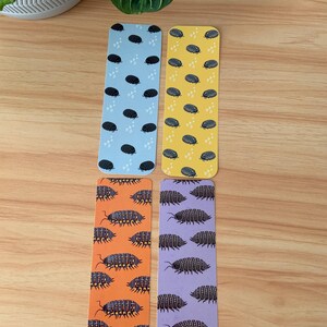 May include: Four colorful bookmarks with insect illustrations. Two bookmarks have a light blue and yellow background with black oval shapes. The other two have orange and purple backgrounds with detailed insect drawings.