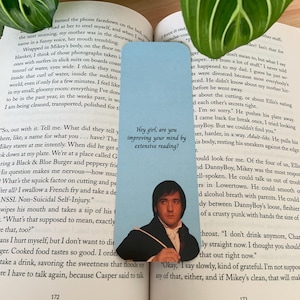 Op de afbeelding: Een lichtblauwe rechthoekige boekenlegger met een afbeelding van een man in een donkere jas en wit overhemd. De tekst "Hey girl, are you improving your mind by extensive reading?" staat in zwarte letters boven de afbeelding van de man.