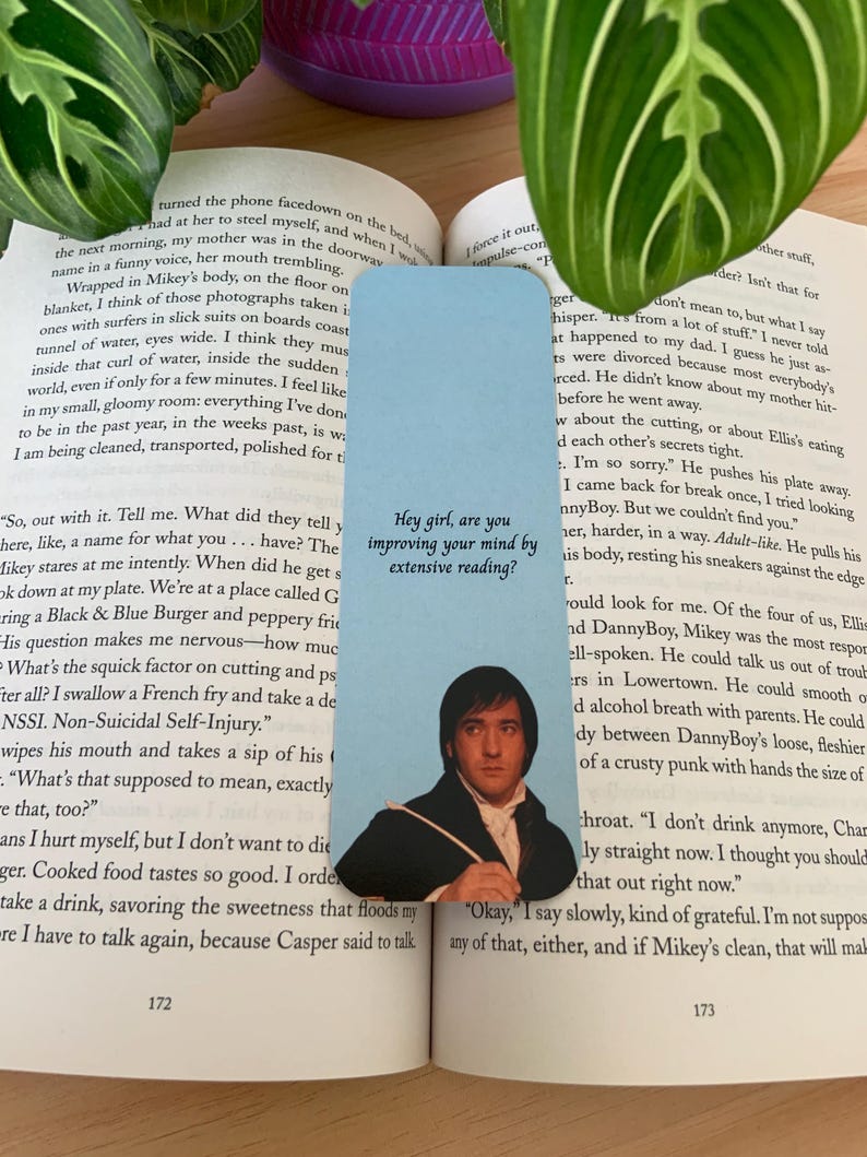 Op de afbeelding: Een lichtblauwe rechthoekige boekenlegger met een afbeelding van een man in een donkere jas en wit overhemd. De tekst "Hey girl, are you improving your mind by extensive reading?" staat in zwarte letters boven de afbeelding van de man.