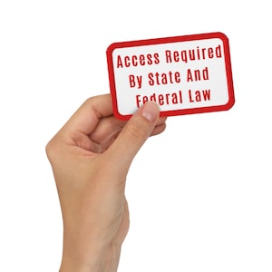 May include: A rectangular white and red sign with rounded corners is held in a hand. The sign reads "Access Required By State And Federal Law" in red text. The sign has a red border and is against a white background.