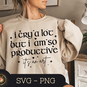 May include: A beige sweatshirt with the text "i cry a lot but i am so PRODUCTIVE it's an art" printed in black. The text is surrounded by small hearts and stars.