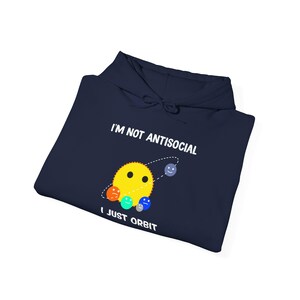 Könnte beinhalten: Marineblauer Kapuzenpullover mit dem Text "I'M NOT ANTISOCIAL I JUST ORBIT". Die Grafik zeigt eine gelbe Sonne mit Gesicht und farbigen Planeten. Der Hoodie ist aus weichem Material.