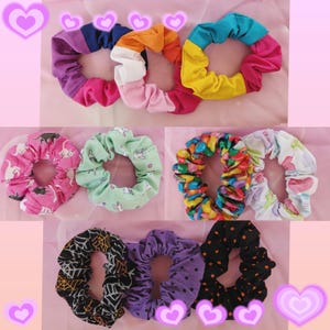 May include: A collection of colorful scrunchies made from fabric with various patterns. The scrunchies include a rainbow pattern, a cat and unicorn pattern, a candy pattern, a purple and black polka dot pattern, and a black and white spiderweb pattern.