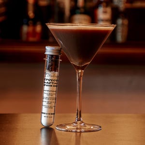 Może przedstawiać: Przezroczysta szklana prob&oacute;wka z ciemnymi ziarnami kawy i białym proszkiem, z etykietą Espresso Martini Infusion Shot, obok kieliszka do martini wypełnionego ciemnobrązowym płynem. Etykieta zawiera instrukcje dla 6-10 drink&oacute;w, waga netto 51 gram&oacute;w.