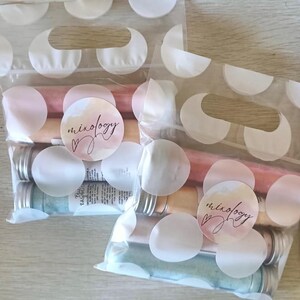Puede incluir: Dos bolsas de plástico transparente con lunares blancos, cada una con varios tubos de vidrio con contenido colorido. Las bolsas tienen una pegatina que dice "mixology" en cursiva. Los tubos tienen tapas plateadas y contienen líquidos rosa, melocotón y azul.