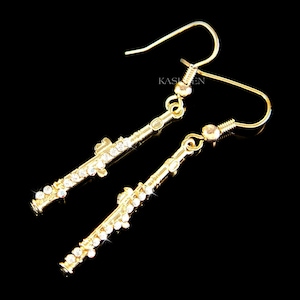 May include: A pair of gold-tone dangle earrings featuring a detailed flute design with clear crystal accents. The earrings have a hook closure.