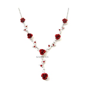 May include: A silver necklace with red rose charms and clear rhinestones. The necklace has a Y-shaped design with a single rose charm dangling from the bottom.
