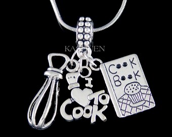 May include: Silver charm necklace featuring a whisk, a heart with the text "I love to cook", and a cookbook charm. The necklace is on a silver chain.