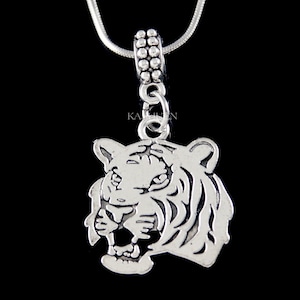 May include: Silver charm necklace with a detailed tiger head pendant. The pendant is silver and has a textured finish.