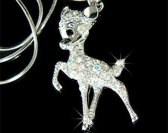 May include: A silver necklace with a crystal-encrusted deer pendant. The deer is standing on all four legs with its head tilted to the side. The necklace is made of a delicate chain.