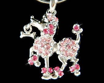 Può includere: Una collana con un ciondolo d'argento con un ciondolo a forma di barboncino di cristallo rosa. Il barboncino è in piedi su tutte e quattro le zampe con la coda arrotolata. Il ciondolo è ricoperto di piccoli cristalli rosa.
