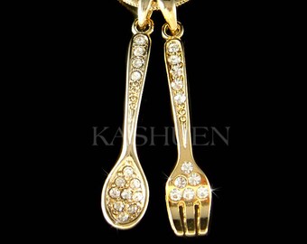 May include: Gold-tone necklace with a spoon and fork pendant, both encrusted with clear sparkling crystals.