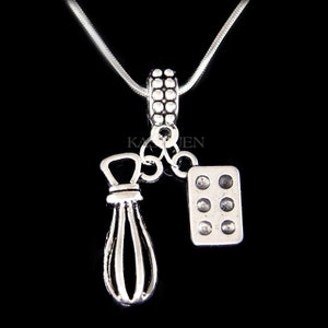 May include: Silver necklace with a charm of a whisk and a baking pan. The necklace is on a silver chain.