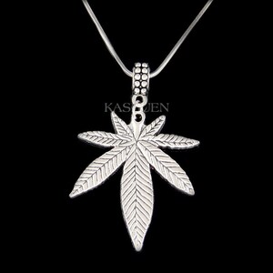 May include: Silver necklace with a detailed marijuana leaf pendant. The pendant is attached to a silver chain.