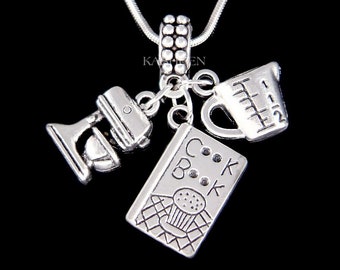 May include: Silver necklace with four charms: a cookbook, a measuring cup, a mixer, and a cupcake. The charms are attached to a silver chain.