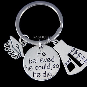 May include: Silver keyring with a graduation cap charm, a round charm with the text "He believed he could, so he did", and a beaker charm with a graduated scale.