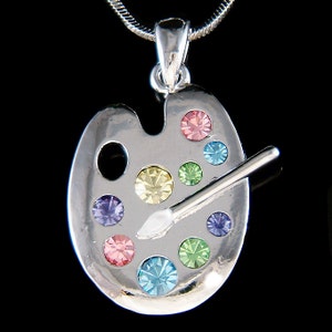 May include: Silver artist's palette pendant necklace with colourful crystal accents. The palette features a paintbrush and a variety of colours, including pink, blue, green, yellow, and purple.