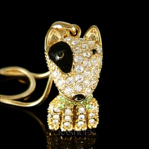 May include: Gold-tone necklace featuring a crystal-encrusted bull terrier pendant. The pendant has black enamel detailing for the eyes and nose, and green crystal accents for the collar.
