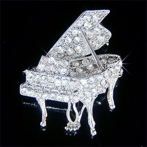 May include: A silver grand piano brooch with a crystal-encrusted design. The piano is open and the lid is decorated with crystals.