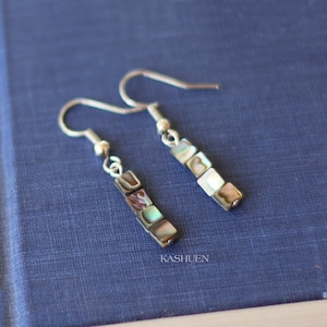 May include: A pair of silver earrings with a dangle design. Each earring features five square-shaped iridescent shell beads.