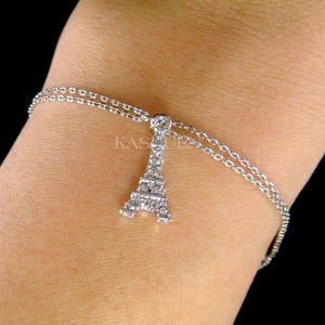 Puede incluir: Un brazalete de cadena plateada con un dije de la Torre Eiffel incrustado de cristales. El brazalete es de doble cadena y tiene una cadena delicada.