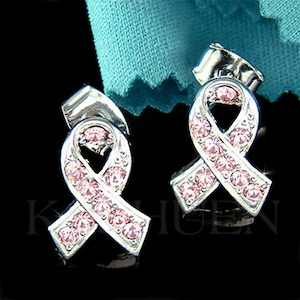May include: A pair of silver earrings with pink crystal ribbon designs. The earrings are a symbol of breast cancer awareness.